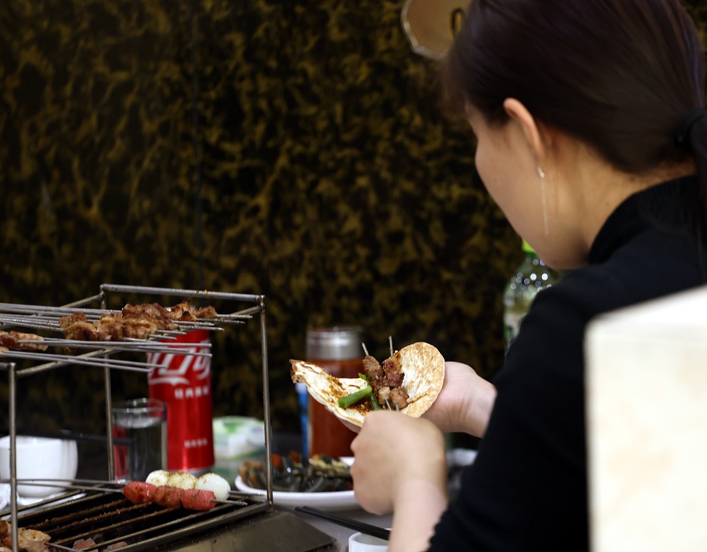 Một thực khách cuộn bánh kếp với hai xiên và hành lá tại nhà hàng thịt nướng ở Truy Bác /CFP